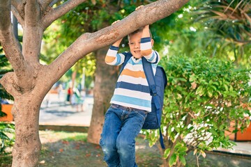 Adorable caucasian student boy smiling happy hanging on tree branch at the park.