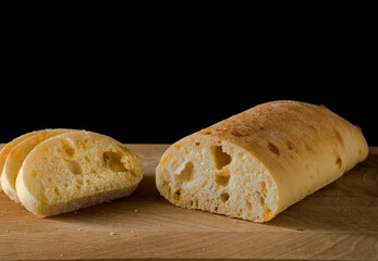 Ciabatta - Italian bread with cheese cut into slices on a wooden board on a black background