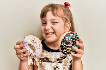 Little caucasian girl kid holding tasty colorful doughnuts winking looking at the camera with sexy...