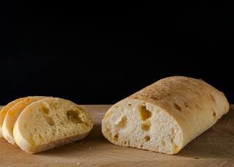 Ciabatta - Italian bread with cheese cut into slices on a wooden board on a black background