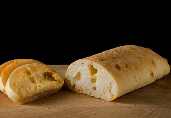 Ciabatta - Italian bread with cheese cut into slices on a wooden board on a black background
