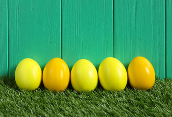 Bright Easter eggs on green grass against wooden background
