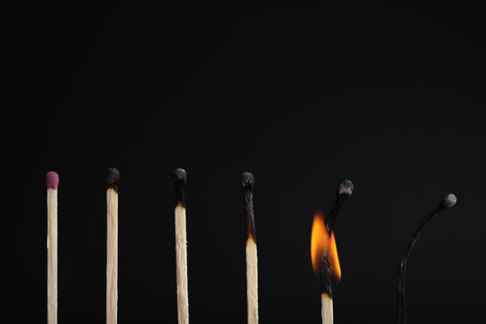 Row of burnt matches and whole one on black background