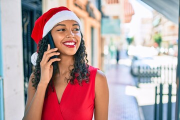 Young african american girl wearing christmas hat talking on the smartphone at city.