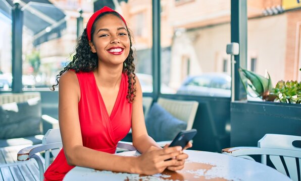 Young african american girl smiling happy using smartphone sitting on the table at coffee shop terrace.