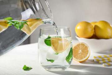 Pouring of refreshing lemonade into glass on white table