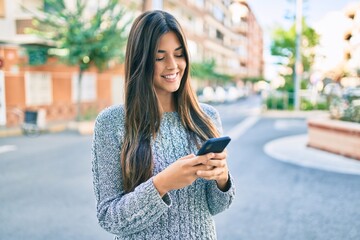 Fototapeta premium Young beautiful hispanic girl smiling happy using smartphone at the city.