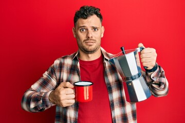 Young hispanic man drinking italian coffee clueless and confused expression. doubt concept.
