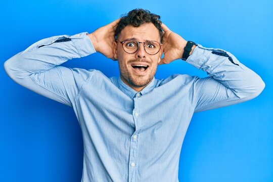 Young hispanic man wearing casual clothes and glasses crazy and scared with hands on head, afraid and surprised of shock with open mouth
