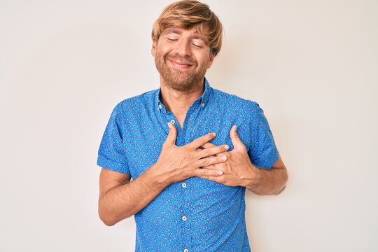 Young blond man wearing casual clothes smiling with hands on chest, eyes closed with grateful gesture on face. health concept.