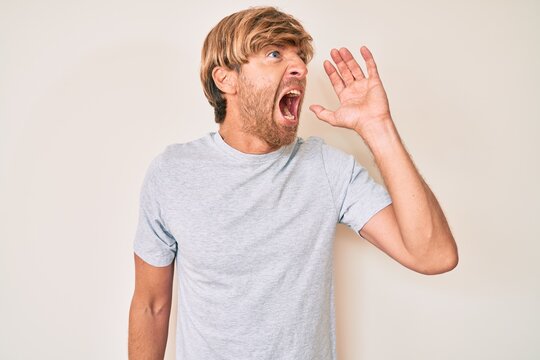 Young blond man wearing casual clothes shouting and screaming loud to side with hand on mouth. communication concept.