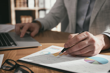 Businessman working with charts and graphs at table in office, closeup. Investment analysis