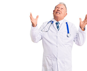 Senior handsome grey-haired man wearing doctor coat and stethoscope crazy and mad shouting and yelling with aggressive expression and arms raised. frustration concept.