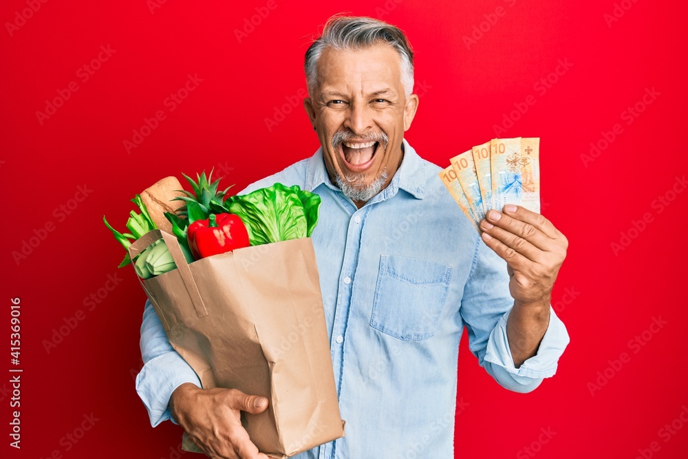 Sticker middle age grey-haired man holding groceries and swiss franc banknotes smiling and laughing hard out