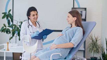 Obraz premium Happy Pregnant Woman Visit Gynecologist Doctor at the Medical Clinic. Female Doctor Examine Pregnant Young Mother to Check Up Her Healthcare. Teenage Pregnancy. Consulting of Pregnant at Clinic.
