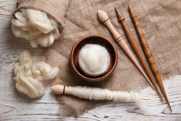 Soft wool and spindles on white wooden table, flat lay