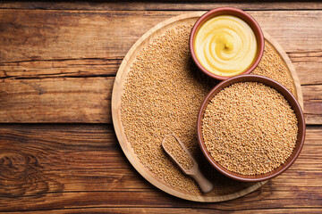 Mustard seeds and sauce on wooden table, top view. Space for text