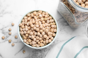 Bowl and jar with chickpeas on white marble table, flat lay