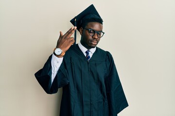 Handsome black man wearing graduation cap and ceremony robe shooting and killing oneself pointing hand and fingers to head like gun, suicide gesture.