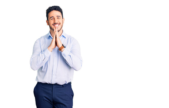 Young hispanic man wearing business clothes praying with hands together asking for forgiveness smiling confident.