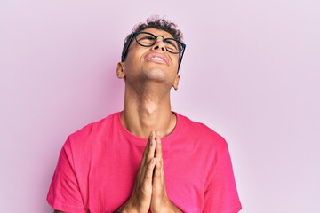 Young handsome african american man wearing glasses over pink background begging and praying with...