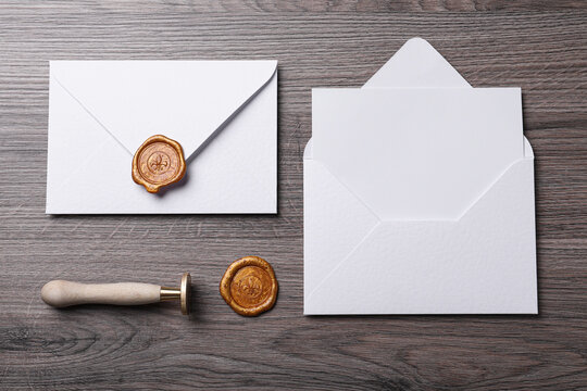 Envelopes with wax seal and stamp on wooden table, flat lay