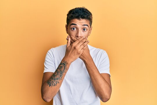 Young handsome african american man wearing casual white tshirt shocked covering mouth with hands for mistake. secret concept.