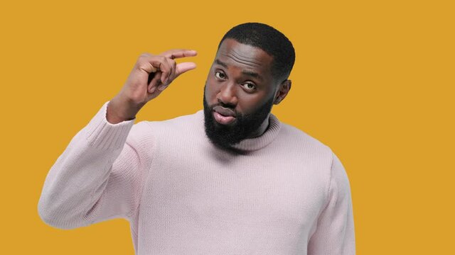 Young handsome black man show something small: Little bit Gesture. on yellow background