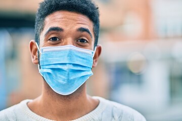 Young african american man wearing medical mask standing at the city.