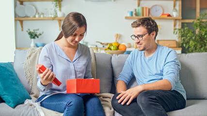 Ordering Gifts Online. A Man Gives a Woman a Gift that He Ordered Through the Site, an Online Store. The Girl Takes Out a Red Gift From a Cardboard Box. Happy Family Time. Enjoy Each Other.
