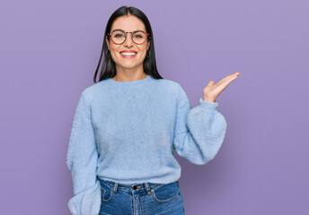 Young hispanic woman wearing casual clothes and glasses smiling cheerful presenting and pointing with palm of hand looking at the camera.