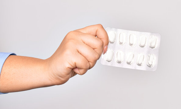 Hand of caucasian young woman holding tablet of pills medicines over isolated white background
