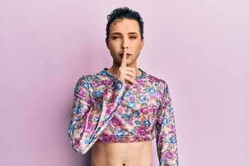 Handsome man wearing make up wearing fashion clothes asking to be quiet with finger on lips....