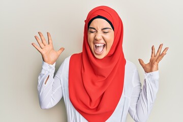 Young beautiful hispanic girl wearing traditional islamic hijab scarf celebrating mad and crazy for success with arms raised and closed eyes screaming excited. winner concept