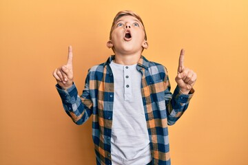 Little caucasian boy kid wearing casual clothes amazed and surprised looking up and pointing with...