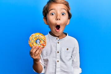 Adorable latin kid holding donut scared and amazed with open mouth for surprise, disbelief face