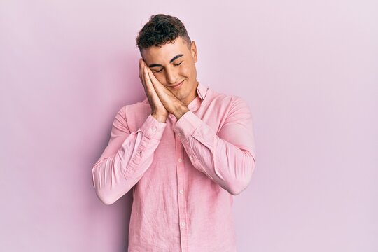 Hispanic young man wearing casual clothes sleeping tired dreaming and posing with hands together while smiling with closed eyes.