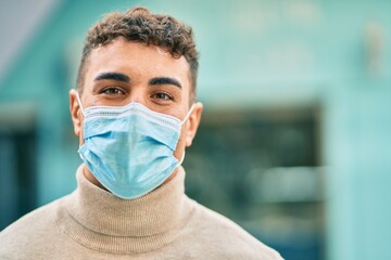 Young hispanic man wearing medical mask standing at the city.