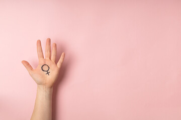 Female hand with female symbol of Venus on pink background for international womens day