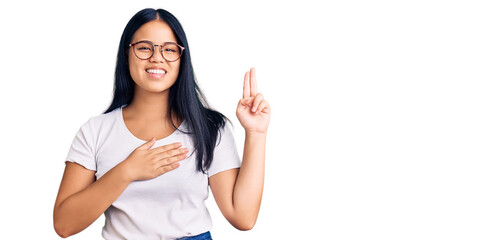 Young beautiful asian girl wearing casual clothes and glasses smiling swearing with hand on chest...