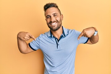 Handsome man with beard wearing casual clothes looking confident with smile on face, pointing...