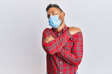 Handsome man with beard wearing medical mask hugging oneself happy and positive, smiling confident. self love and self care