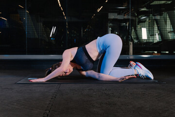 Charming young slim woman doing yoga. She wears a black sports bra and blue tights. She is doing sport exercises on yoga mat. Sexy woman doing yoga in the gym.