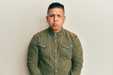 Fototapeta premium Young latin man wearing casual clothes puffing cheeks with funny face. mouth inflated with air, crazy expression.