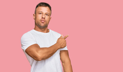 Handsome muscle man wearing casual white tshirt pointing with hand finger to the side showing...
