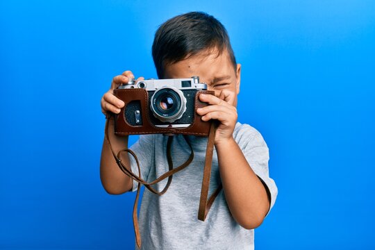 Adorable latin photographer toddler smiling happy using vintage camera over isolated blue background.