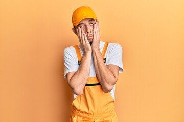 Hispanic young man wearing handyman uniform tired hands covering face, depression and sadness, upset and irritated for problem