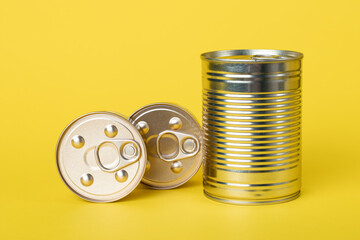 Canned food on a yellow background, closed shiny golden cans. Tinned goods. Metallic jars. Preserves, conserve.