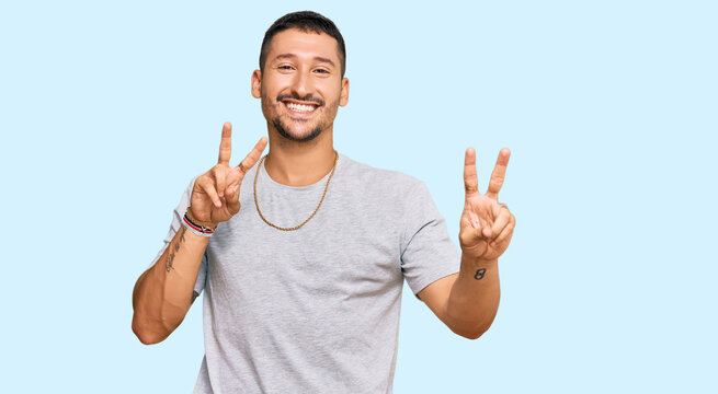 Handsome man with tattoos wearing 90s style smiling looking to the camera showing fingers doing victory sign. number two.
