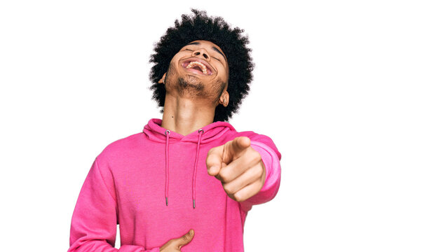 Young african american man with afro hair wearing casual pink sweatshirt laughing at you, pointing finger to the camera with hand over body, shame expression